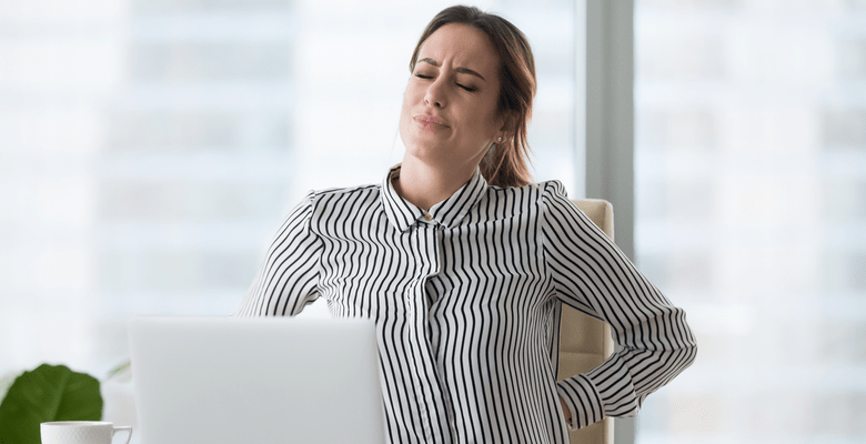 Eine Frau verzieht im Homeoffice ihr Gesicht aufgrund Rückenschmerzen