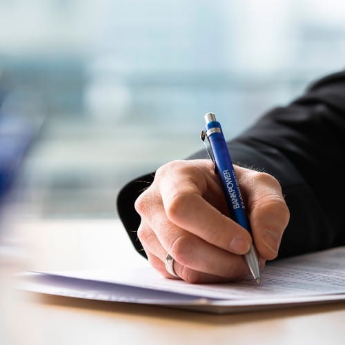 Hand mit einem Stift in der Hand, die auf darunter liegenden Dokumenten schreibt
