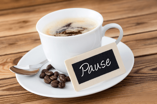 Eine Tasse Kaffee, mit Kaffeebohnen und Pause-Schild am Tellerrand