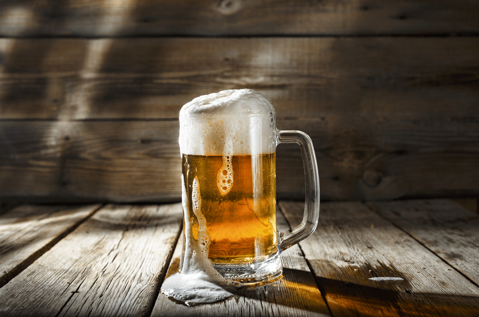Bierkrug aus Glas mit frisch gezapftem Bier, dessen Krone etwas überläuft